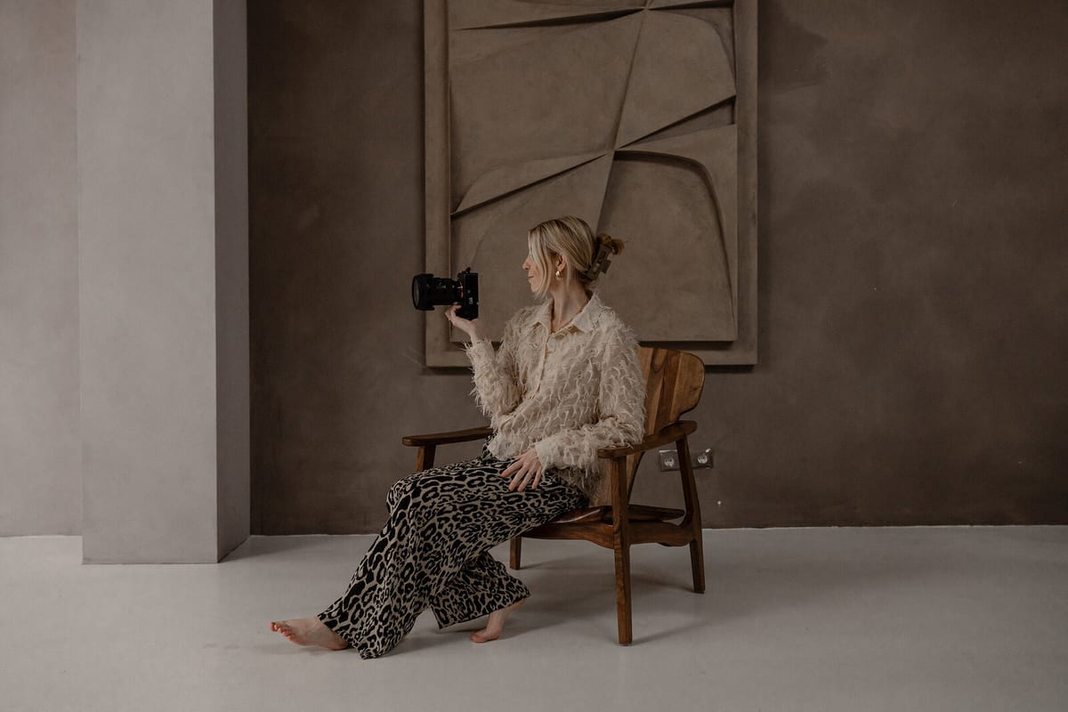 Romy van Leeuwen zit op een houten stoel en houdt haar camera opzij in een warme studio