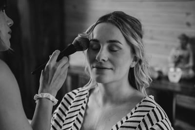 Femke sluit haar ogen terwijl de visagiste haar make-up aanbrengt tijdens de voorbereidingen, in zwart-wit