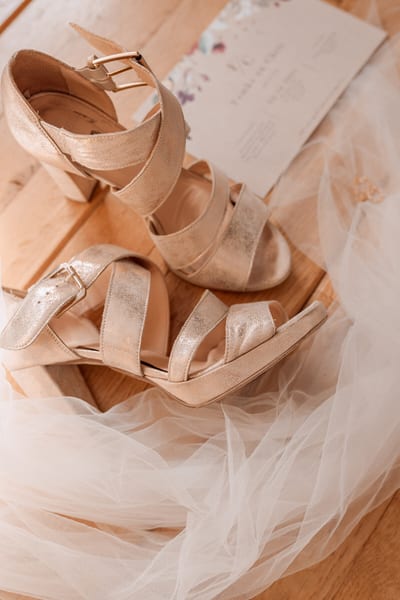De goudkleurige trouwschoenen van Femke liggen naast de sluier en de trouwkaart op een houten vloer