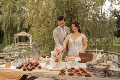 Dominique en Daimy snijden samen de bruidstaart aan bij een tafel vol gebakjes in de tuin