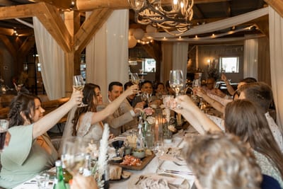 Dominique en Daimy proosten met hun gasten aan een lange dinertafel onder lichtslingers en witte draperieën
