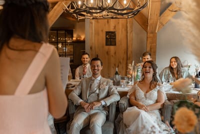 Dominique en Daimy zitten lachend naast elkaar te luisteren naar een toespraak in een warme zaal met houten wanden