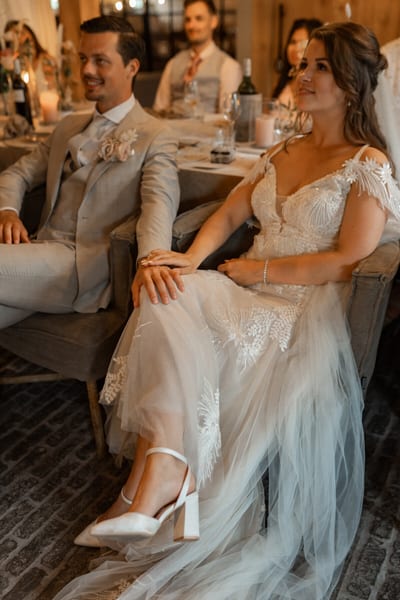 Dominique en Daimy zitten dicht naast elkaar in fauteuils tijdens het diner, met kaarslicht en gasten aan tafel achter hen