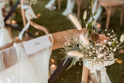 Naamkaartje en veldboeketje met droogbloemen op een houten stoel bij de buitenceremonie van Danny en Esmee