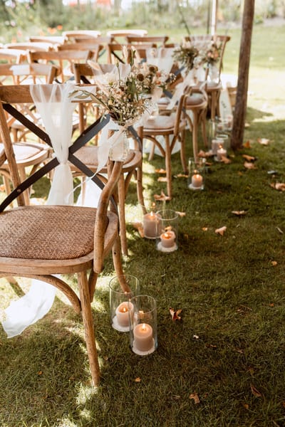 Houten stoelen met droogbloemen, doeken en kaarsen in glas markeren het gangpad voor de buitenceremonie van Danny en Esmee