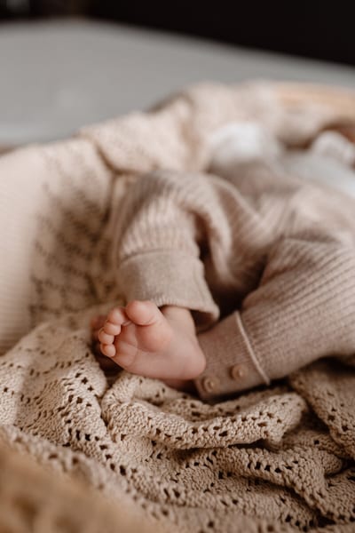 Voetjes van een pasgeboren baby steken uit een gebreid beige pakje, liggend op een zachte kanten deken