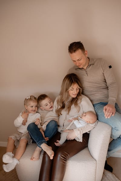 Ouders en hun twee kinderen zitten samen op de bank rond de pasgeboren baby tijdens de newbornshoot