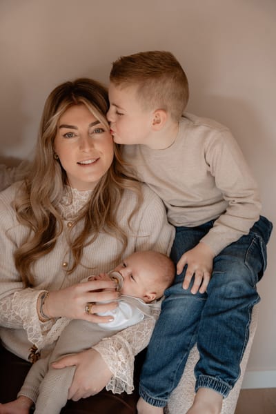 Grote broer kust zijn moeder op het hoofd terwijl zij de pasgeboren baby met speentje in haar armen wiegt