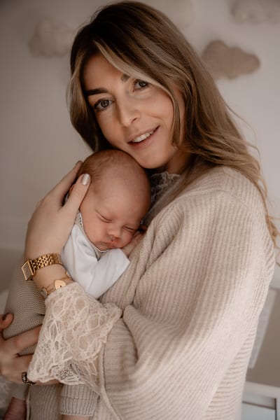 Moeder vlijt haar wang tegen het hoofdje van haar slapende newborn, gehuld in zachte beige tinten