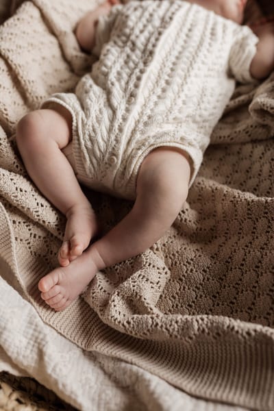 Beentjes en voetjes van een pasgeboren baby in een gebreid pakje op zachte dekens in warme tinten