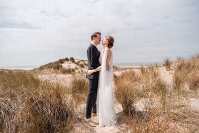 Mart en Loes staan tegenover elkaar tussen het helmgras in de duinen, met de zee in de verte