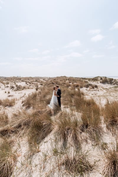 Mart en Loes kussen elkaar midden in een weids duinlandschap vol helmgras, klein onder de open lucht