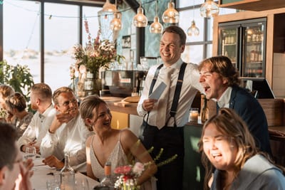 Bruid en gasten lachen om een voorgelezen speech tijdens het diner op de bruiloft van Mart en Loes