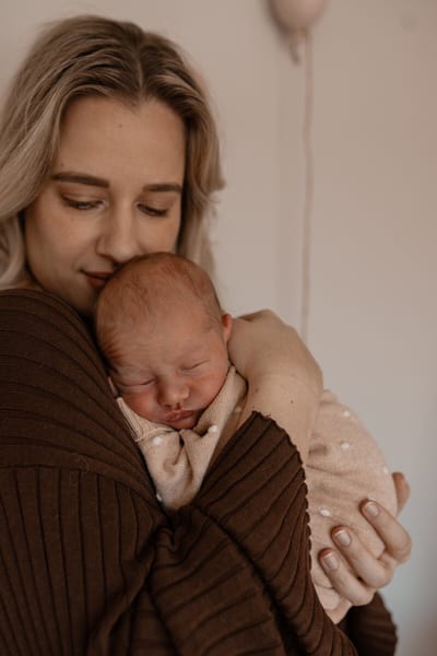 Moeder sluit haar ogen en drukt haar gezicht tegen het hoofdje van haar slapende baby in een gestippeld pakje