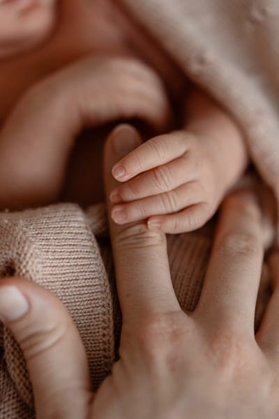 Handje van een pasgeboren baby rust op de vinger van een ouder, omringd door zachtroze dekentjes