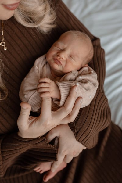Pasgeboren baby slaapt in de armen van de moeder met een handje stevig om haar vinger geklemd