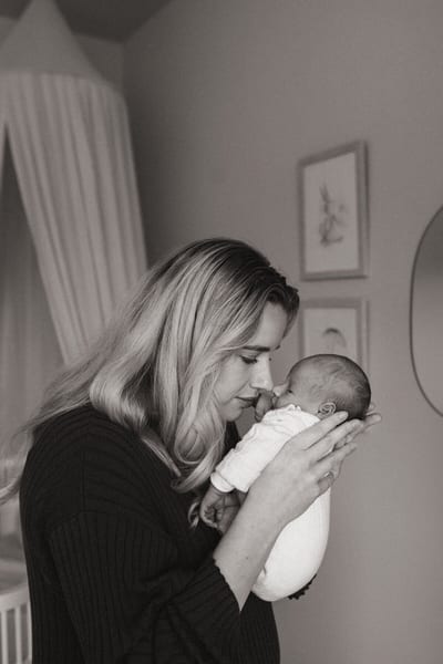 Moeder houdt haar pasgeboren baby vlak bij haar gezicht in de kinderkamer, een teder moment in zwart-wit
