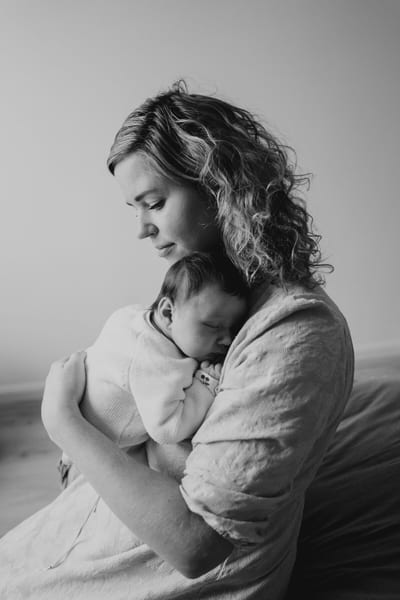 Moeder wiegt haar slapende pasgeboren baby tegen haar schouder, een rustig zwart-witportret bij daglicht