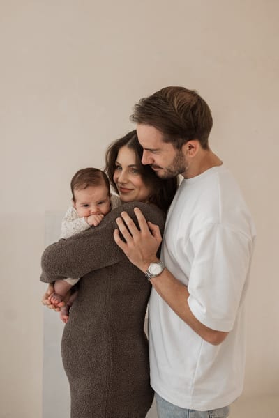 Ouders houden elkaar vast terwijl hun baby over de schouder van de moeder nieuwsgierig de kamer in kijkt