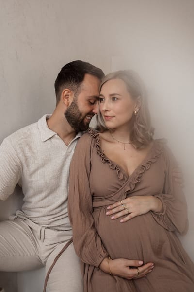 Aanstaande ouders zitten dicht tegen elkaar, zij houdt haar buik vast terwijl hij zijn gezicht naar haar toe buigt