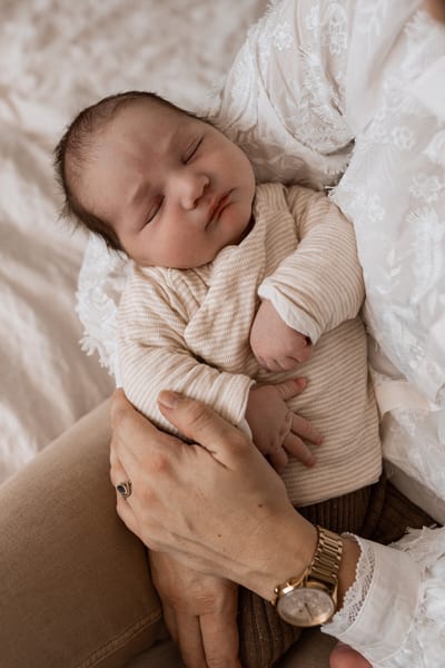 Slapende pasgeboren baby in een gestreept pakje op schoot, de hand van de moeder beschermend om het kindje