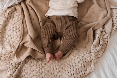 Babyvoetjes steken uit een bruin gebreid broekje, van bovenaf gefotografeerd op zachte gebreide dekens