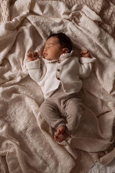 Pasgeboren baby slaapt met de armpjes omhoog in een wit vestje, liggend op laagjes zachte doeken