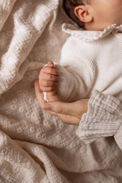 Handje van een pasgeboren baby rust in de open hand van een ouder op een zacht wit dekentje