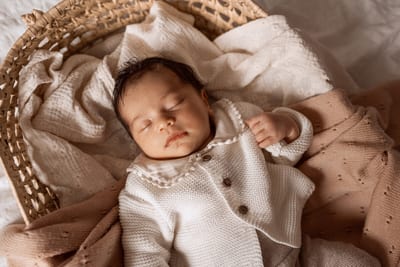 Pasgeboren baby slaapt in een gebreid vestje in een rieten mandje tussen zachte roze dekentjes