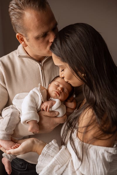 Vader kust het voorhoofd van de moeder terwijl zij hun slapende baby kust, dicht tegen elkaar in warm licht
