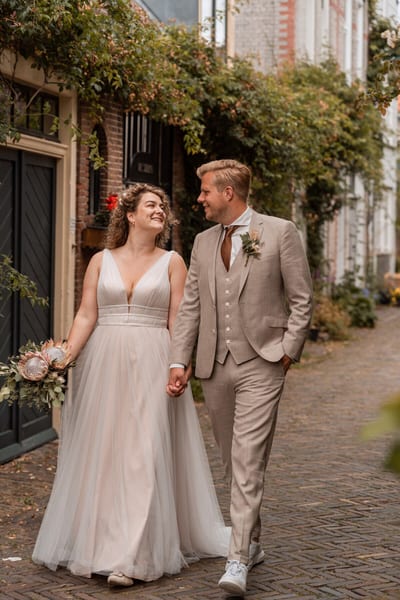 Thijs en Lois wandelen hand in hand door een smal straatje met begroeide oude gevels, elkaar lachend aankijkend