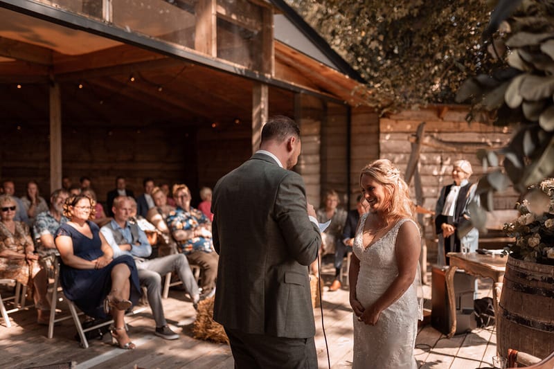 A groom reads his vows while the bride listens and the guests look on from under the veranda